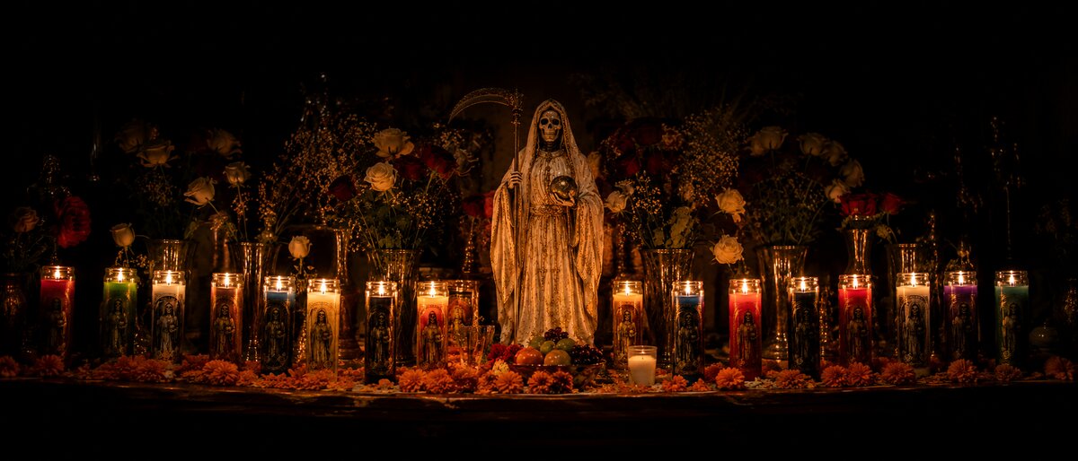 Altar tradicional a la Santa Muerte con veladoras de colores, flores y ofrendas